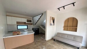 A modern kitchen with a built-in island, a dining area with a bench, and a staircase leading to an upper level. - D'Jiwa by Semesta Management (Turi)