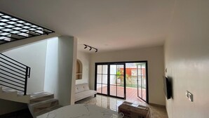 A modern interior with a staircase, a sofa, a sliding glass door, and a marble table. - D'Jiwa by Semesta Management (Turi)