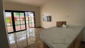 A spacious room with a marble countertop, a flat-screen TV mounted on the wall, and a sliding glass door leading to an outdoor area. - D'Jiwa by Semesta Management (Turi)
