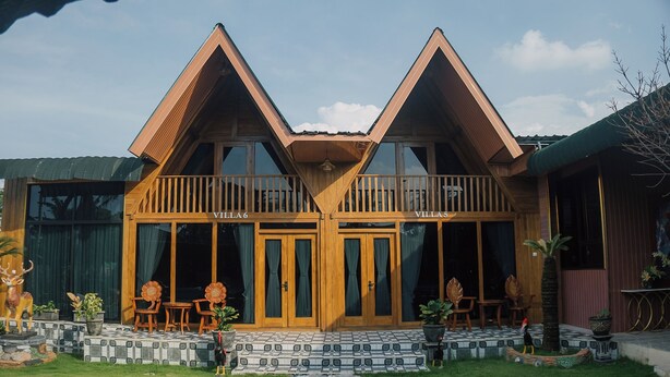 A two-story wooden villa with a balcony, a covered entrance, and a paved pathway leading to the entrance.