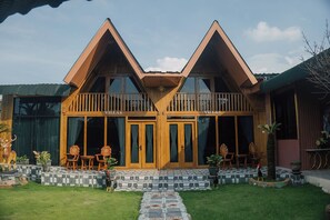 Eine zweistöckige Holzvilla mit Balkon, überdachter Veranda und einem gepflasterten Weg zum Eingang.