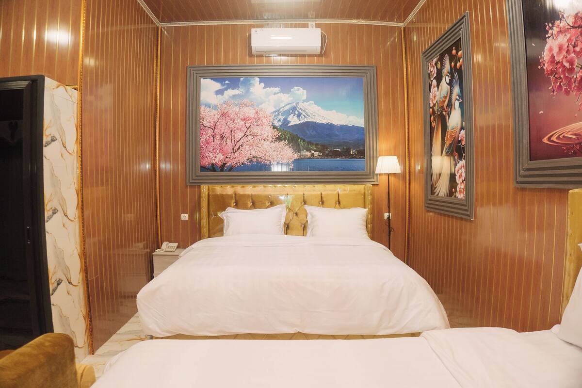 Quarto de hotel com uma cama grande, cabeceira de madeira, pintura do Monte Fuji e uma obra de arte emoldurada com pássaros.