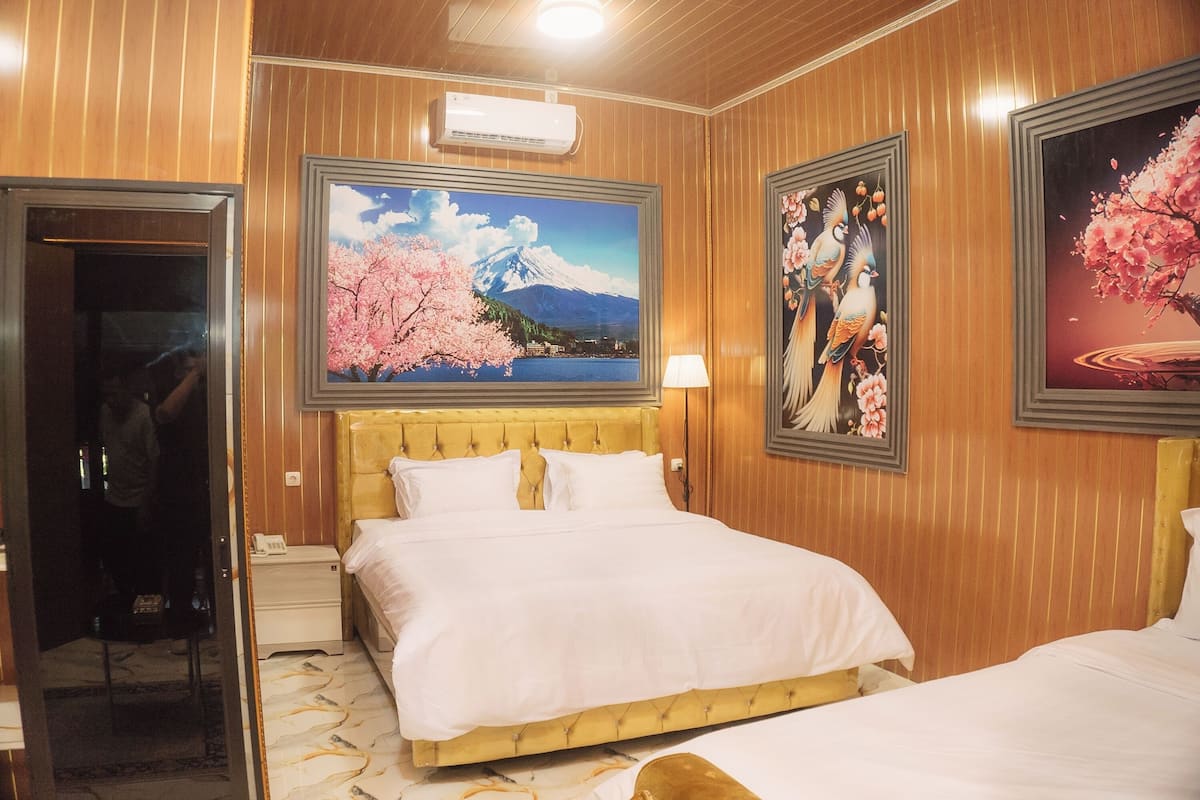 Quarto de hotel com cama, cabeceira de madeira, pintura de montanha e obra de arte emoldurada com pássaros.