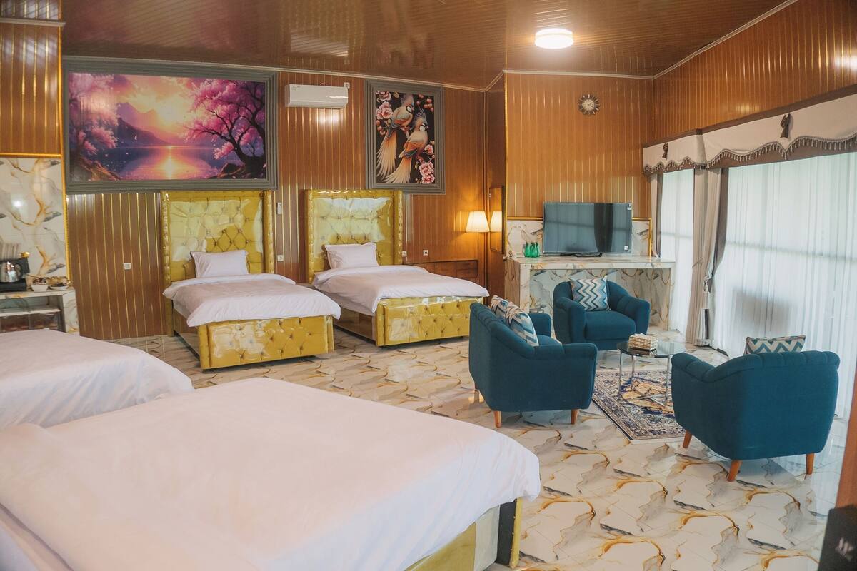 Quarto de hotel com duas camas, uma televisão, um sofá e um painel decorativo.