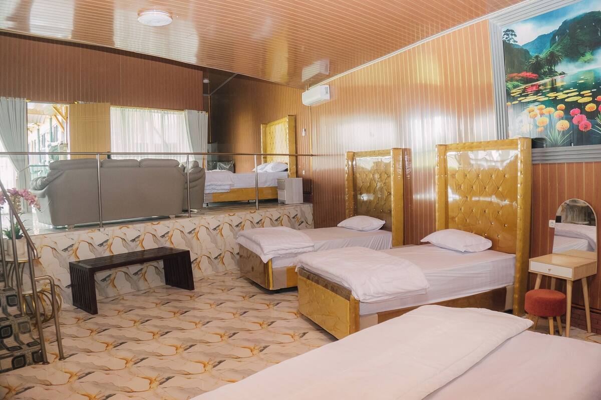Quarto de hotel com três camas, um banco, uma mesinha e um espelho.