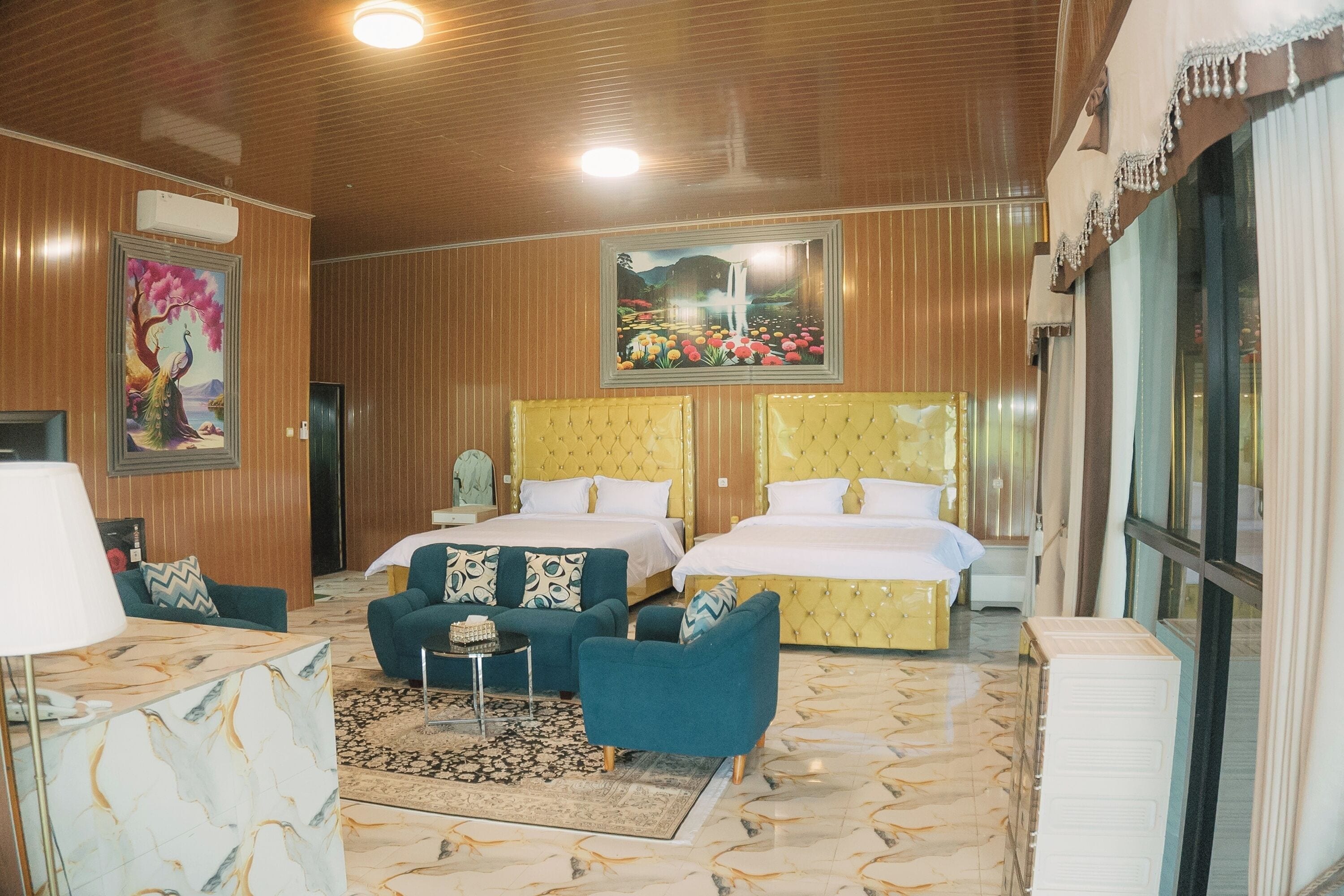 A hotel room with two beds, a sitting area with a sofa and armchairs, a small table, and a large window.
