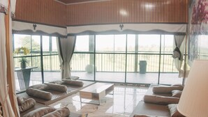 A spacious room with a large window, a sofa set, a coffee table, and a lamp.