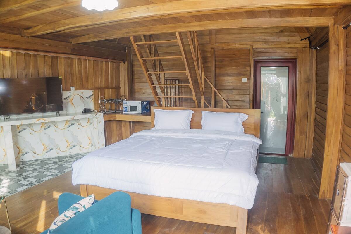 Quarto de cabana de madeira com uma cama, uma escrivaninha com um computador, uma cadeira e uma escada.