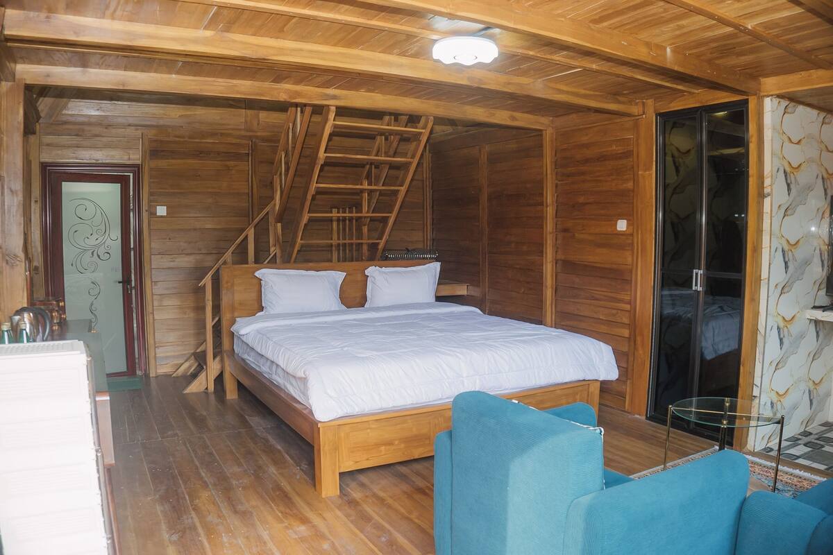 Quarto de cabana de madeira com cama, escada, porta de vidro e uma pequena mesa.