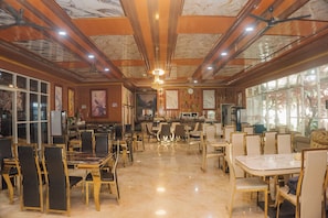 Un restaurant spacieux doté de nombreuses tables et chaises, d’un bar et d’un plafond orné de poutres en bois et de lustres.