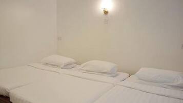 Una habitación con dos camas individuales, ropa de cama blanca, una lámpara fijada a la pared y una pared blanca lisa.