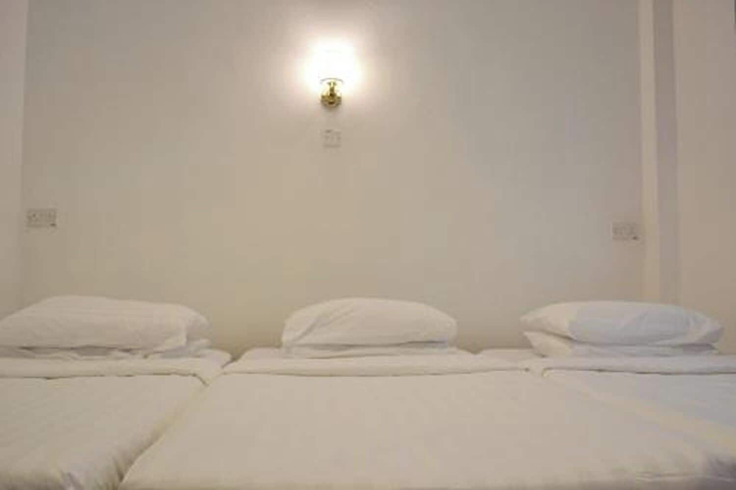 A room with three beds, a wall-mounted light fixture, and a plain wall.