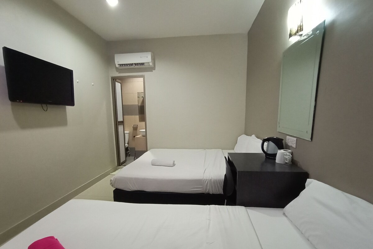 A hotel room with a bed, a desk with a chair, a flat-screen TV, an air conditioning unit, and a bathroom visible through an open door.