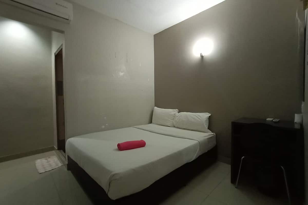 Une petite pièce simple, avec un lit, un bureau et un appareil de climatisation.