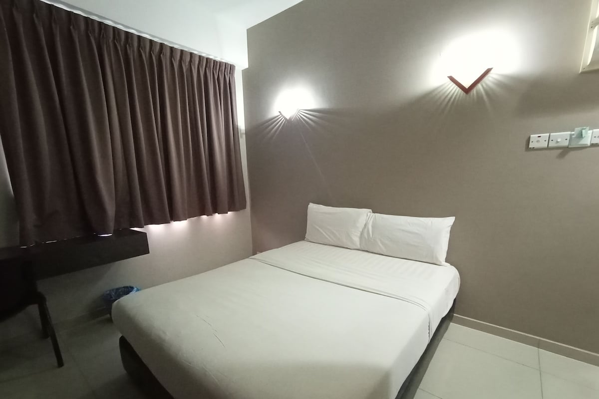 A hotel room with a bed, curtains, a desk, and wall-mounted lights.