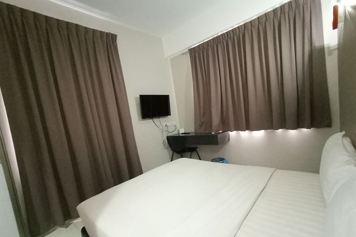 A hotel room with a bed, curtains, a TV, and a desk.