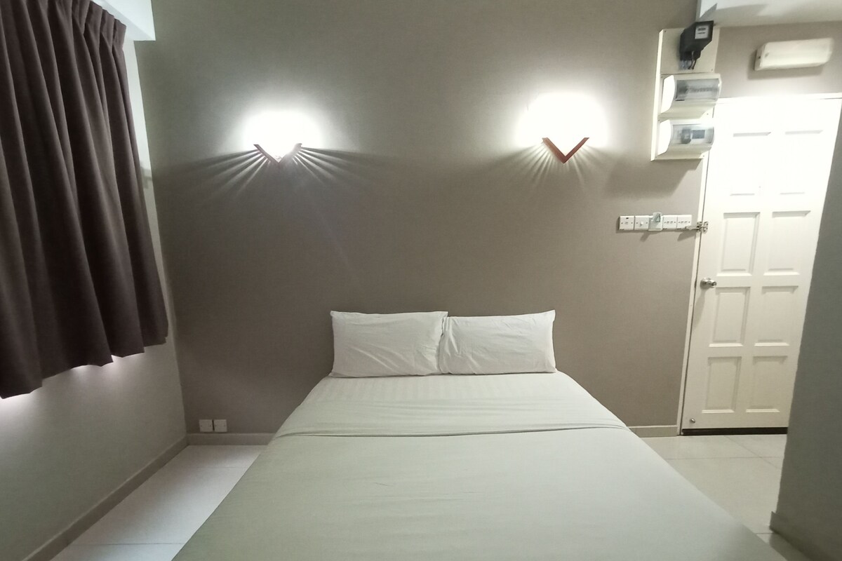 A single bed with white bedding in a room with two wall-mounted lights, a door, and a small shelf with items.