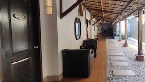 A corridor with a wooden ceiling, a black door, and a seating area with chairs.