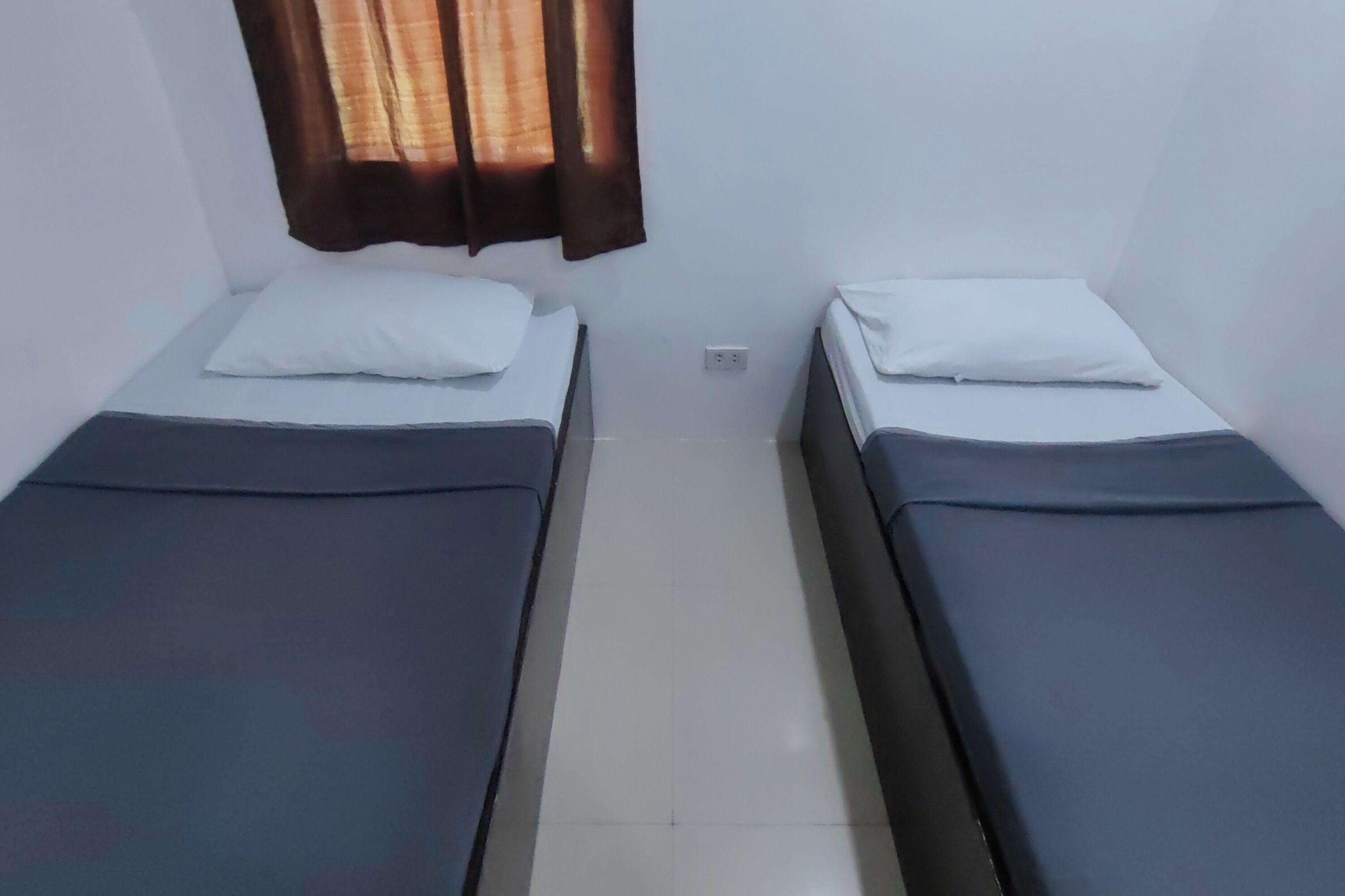 Een kamer met twee eenpersoonsbedden, een raam met gordijnen en een vloer van witte tegels.