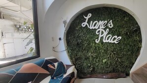 A room with a sofa, a wall-mounted sign reading 'Liane's Place,' and a green wall with a textured design.