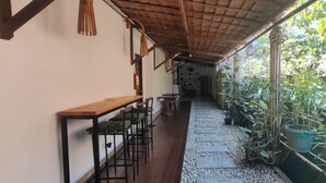 A covered outdoor area with a wooden table and chairs, a fire extinguisher, and potted plants along a stone pathway.