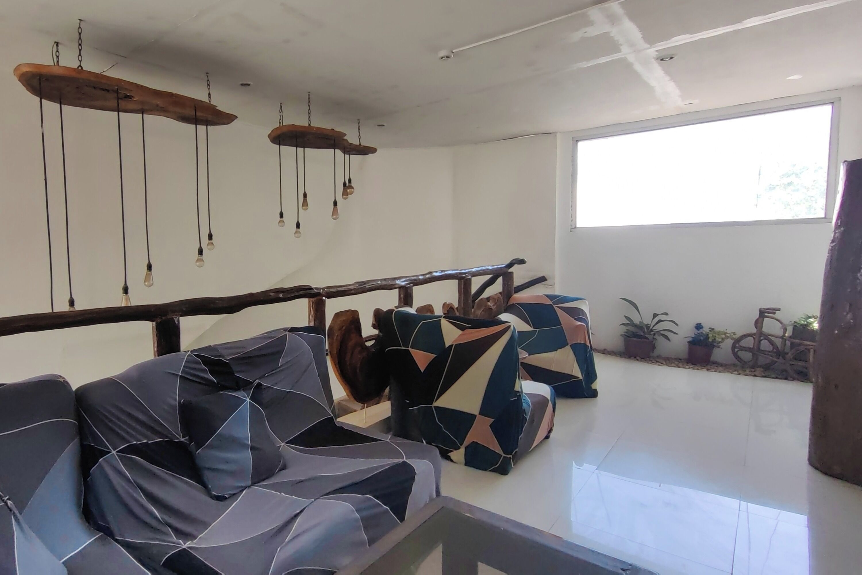 Un espacio de sala moderno con un conjunto de sofás, lámparas colgantes y un ventanal que ofrece luz natural.