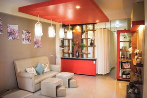 A living room with a sofa, ottomans, a coffee table, pendant lights, a red accent wall, and a bookshelf. - Apihap Hotel (Daraga)