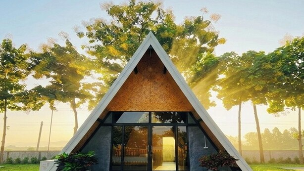 Un edificio moderno de forma triangular con entrada de vidrio, rodeado de árboles y un cielo despejado.