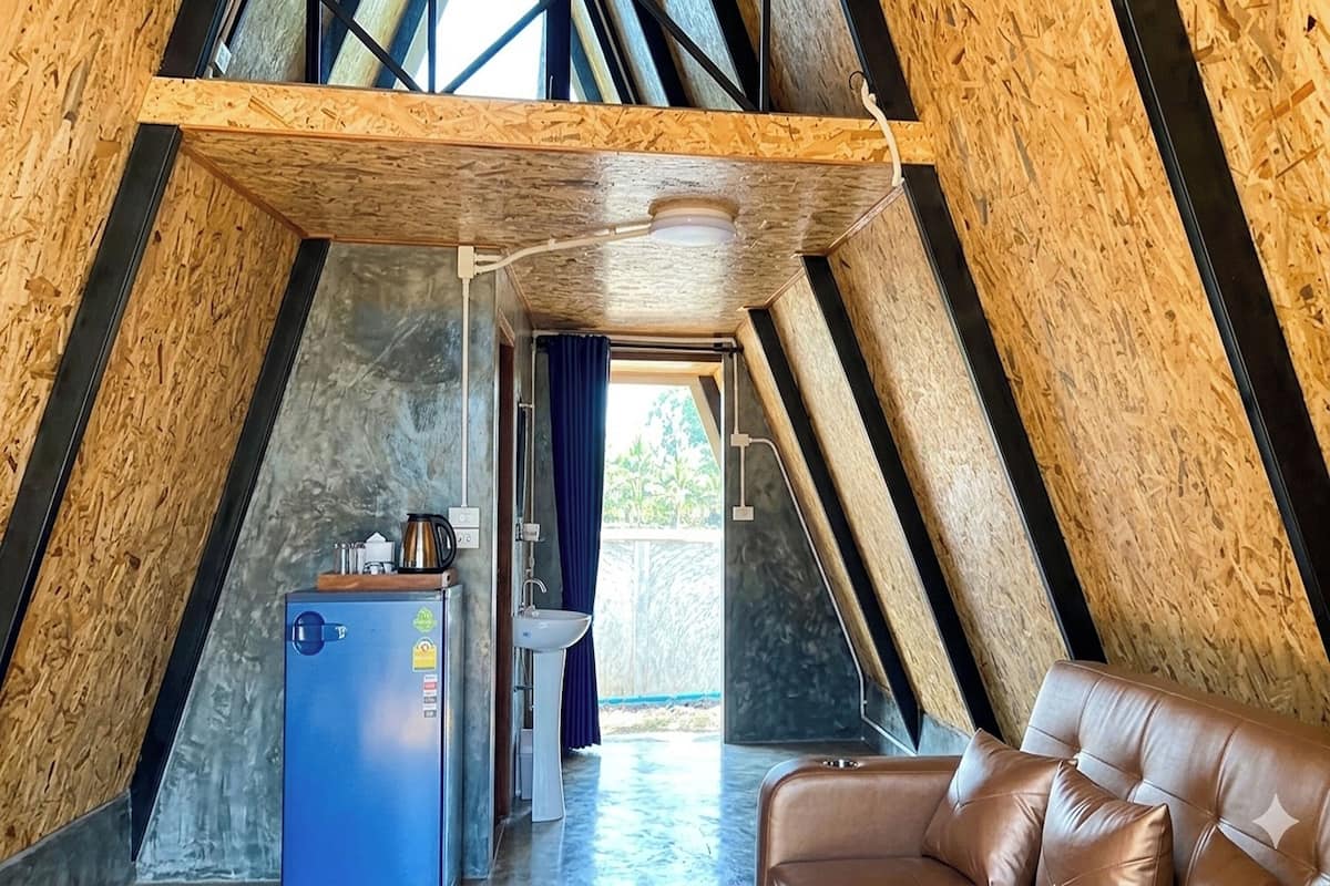 A room with a sloped ceiling, a refrigerator, a sink, and a leather sofa.