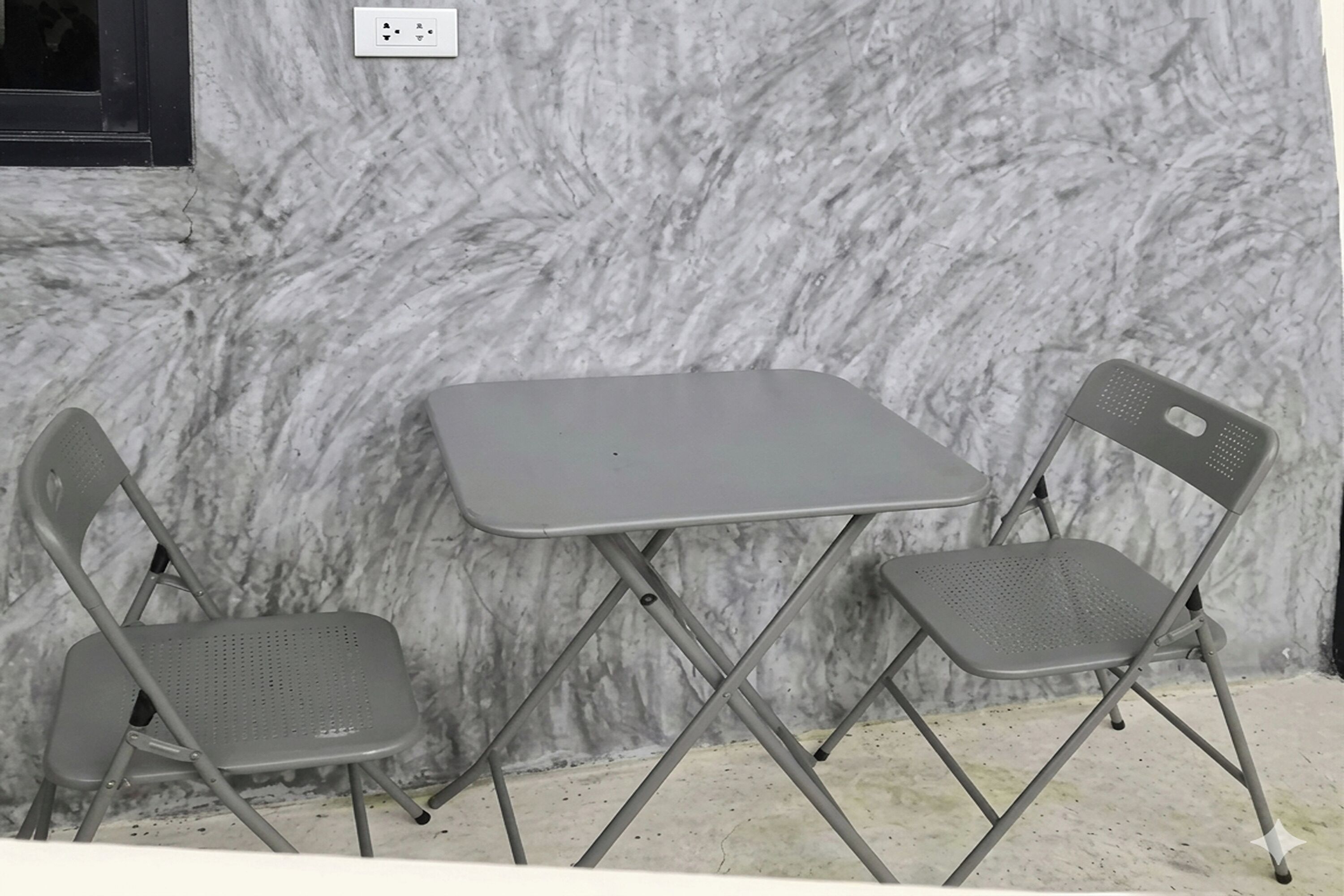 A room with a marble wall, a small table, and two foldable chairs.