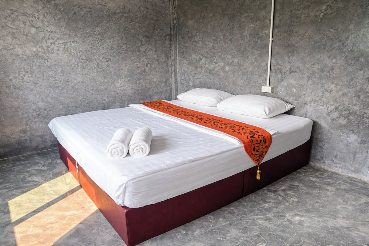 A single bed with white linens, a red headboard, and an orange throw blanket.