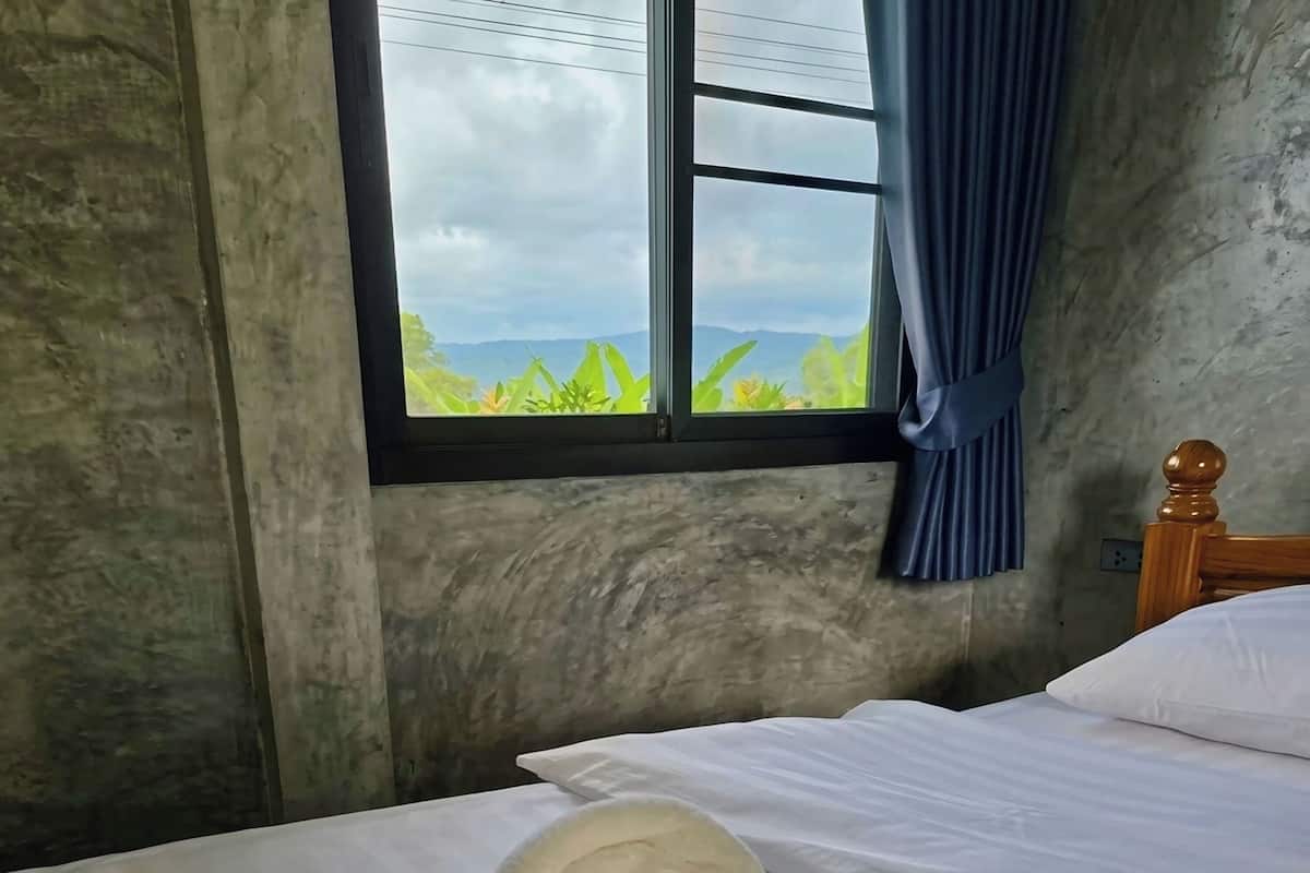 A room with a bed, a window with curtains, and a view of greenery.