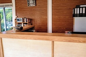 Una recepción con encimera de madera, un reloj, una estantería y un cartel con el símbolo de prohibido fumar.