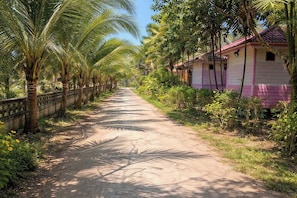 A narrow dirt road flanked by palm trees and a row of pink and white buildings. - Phetmanee Resort (Ko Yao)