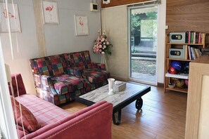 Una sala de estar con un sofá colorido, un sillón rojo, una mesa de centro y una estantería con libros y balones deportivos.