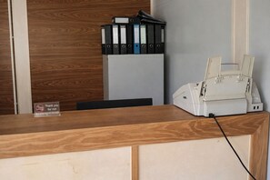 Un mostrador de recepción con detalles de madera, una impresora y una pila de archivadores negros y azules.