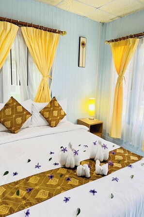 A hotel room with a bed, curtains, pillows, a nightstand with a lamp, and a wall-mounted picture. - Phetmanee Resort (Ko Yao)