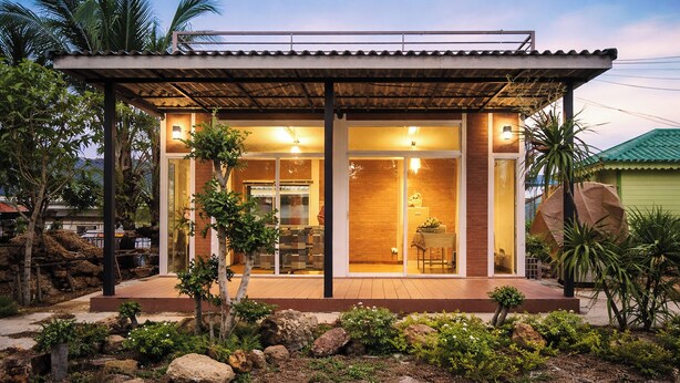 Une maison moderne dotée d’un porche abrité, d’un coin repas et d’une cuisine visible à travers les portes vitrées.