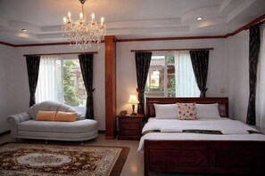A bedroom with a bed, a sofa, a chandelier, and a nightstand. - Lay De Bua Resort (Khuan Khanun)