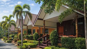 Eine Reihe von Hotelzimmern im Bungalowstil mit Ziegeldächern, Holzbalkonen und einem Kiesweg.