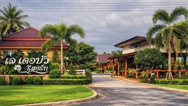 Ein Hotel mit rotem Ziegeldach, Palmen und einem Schild mit thailändischen Schriftzeichen.
