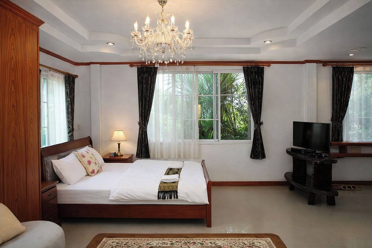 Een slaapkamer met een groot bed, een tv-meubel, een kroonluchter en een raam met gordijnen.