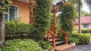 Una scala in legno che conduce all'ingresso di un edificio, circondata da vegetazione rigogliosa e piante in vaso.