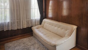 Una stanza con un divano in pelle color beige, pavimento in legno, tappeto bianco e una finestra con tende leggere.