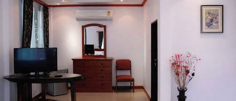 A hotel room with a television, a dresser, a chair, a mirror, an air conditioning unit, and a framed picture on the wall.