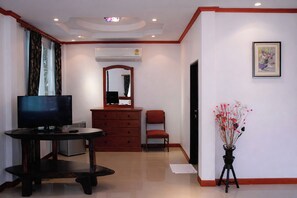 Quarto de hotel com televisão, penteadeira, cadeira, espelho, ar condicionado e quadro na parede.