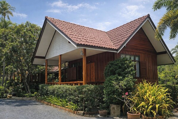 A wooden house with a tiled roof, surrounded by lush greenery and palm trees.