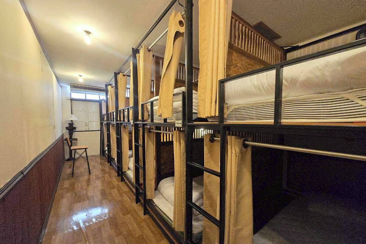 A corridor with bunk beds, wooden partitions, a chair, and a window.
