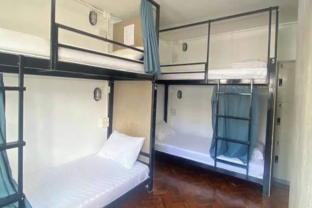 A bunk bed room with wooden flooring, a window with a curtain, and a door.