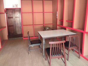 A room with a wooden door, a table, two chairs, and red shelving units. - Nearthepark Backpack Hostel Night Bazaar (Chiang Mai)